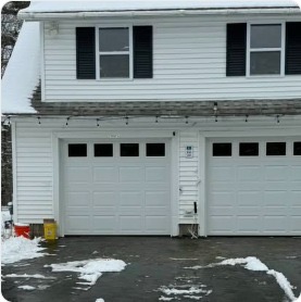 Twin white garage doors installed on residence, snow on ground